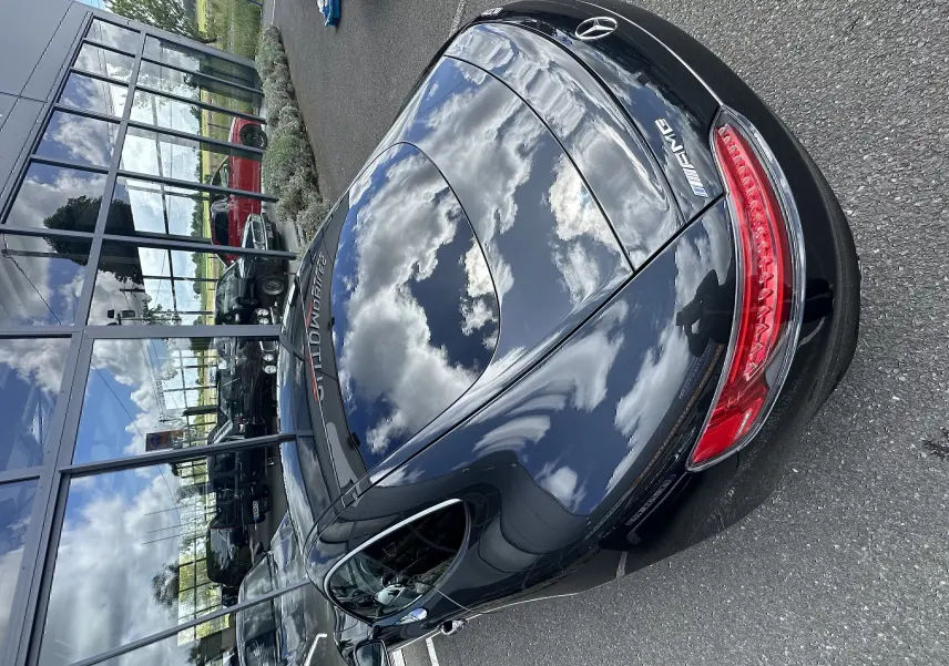 Vue 3/4 arrière d'une Mercedes AMG GT gris foncé brillant, avec feux arrière LED et logo AMG visible.