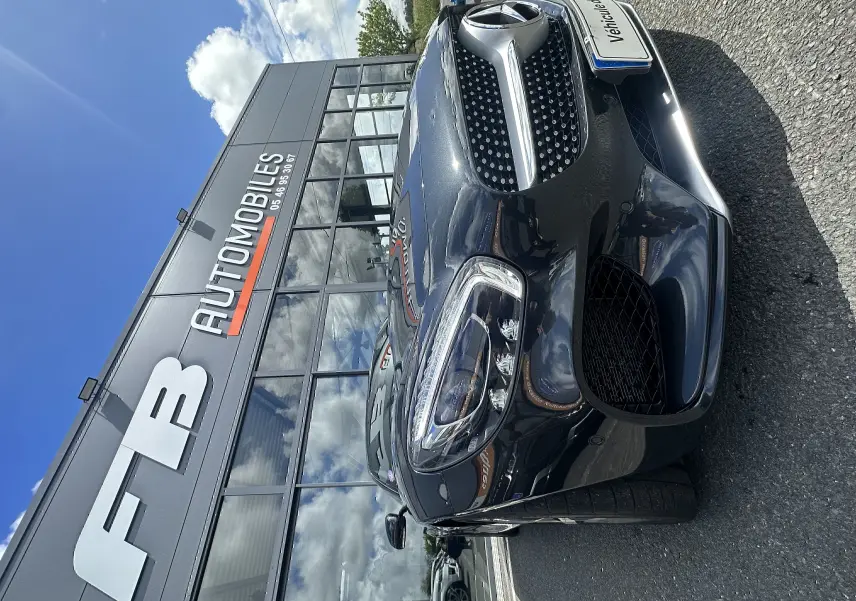 Vue 3/4 avant droit d'une Mercedes AMG GT gris foncé brillante devant un bâtiment de concession automobile.