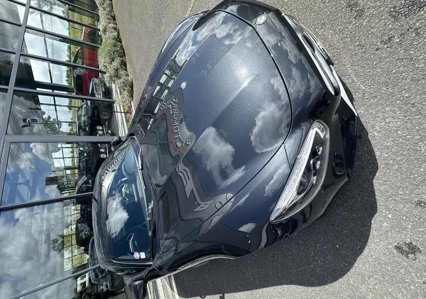 Vue 3/4 avant d'une Mercedes AMG GT gris foncé brillant, avec capot profilé et phares LED distinctifs.