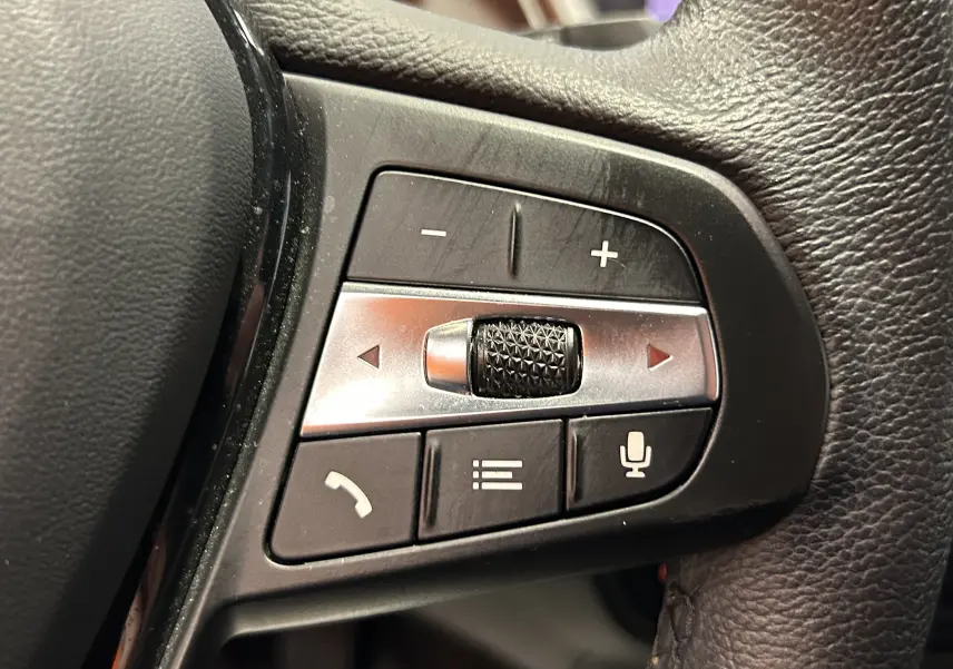 Gros plan sur les commandes multifonctions noires et argentées du volant d'une BMW Série 1 16d noire de 2023.