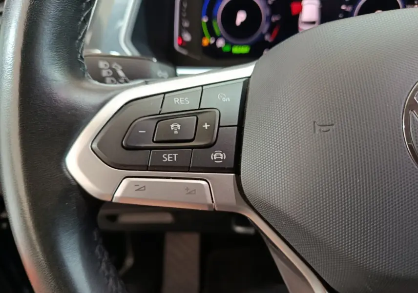 Gros plan sur les commandes gauche du volant cuir du Volkswagen Tiguan hybride rechargeable 2022, affichage numérique en arrière-plan.