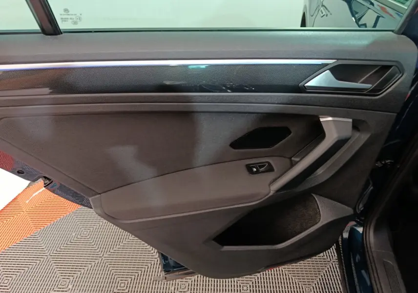 Porte intérieure côté gauche du Volkswagen Tiguan bleu 2022, avec habillage noir et insert décoratif brillant.