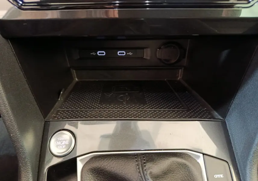 Gros plan sur la console centrale du Volkswagen Tiguan bleu, montrant le bouton start/stop et ports USB lumineux.