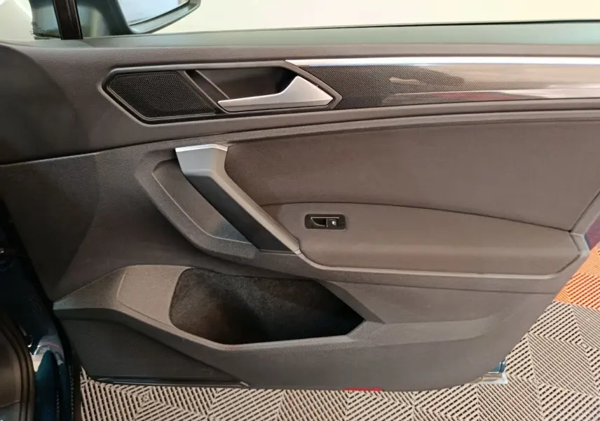 Intérieur côté gauche de la porte du Volkswagen Tiguan bleu 2022, avec poignée argentée et garniture noire.