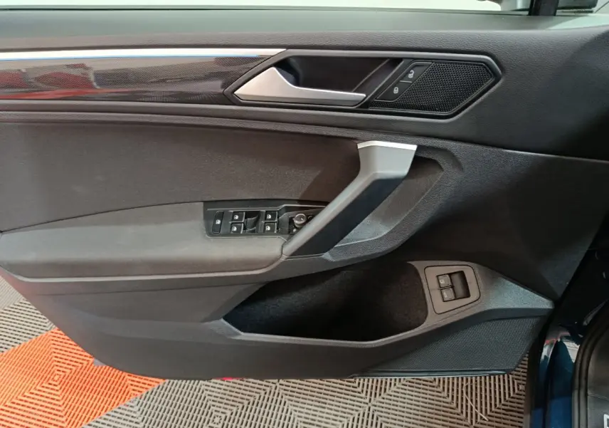 Vue du panneau de porte côté conducteur du Volkswagen Tiguan bleu 2022 avec commandes électriques et finition noire.