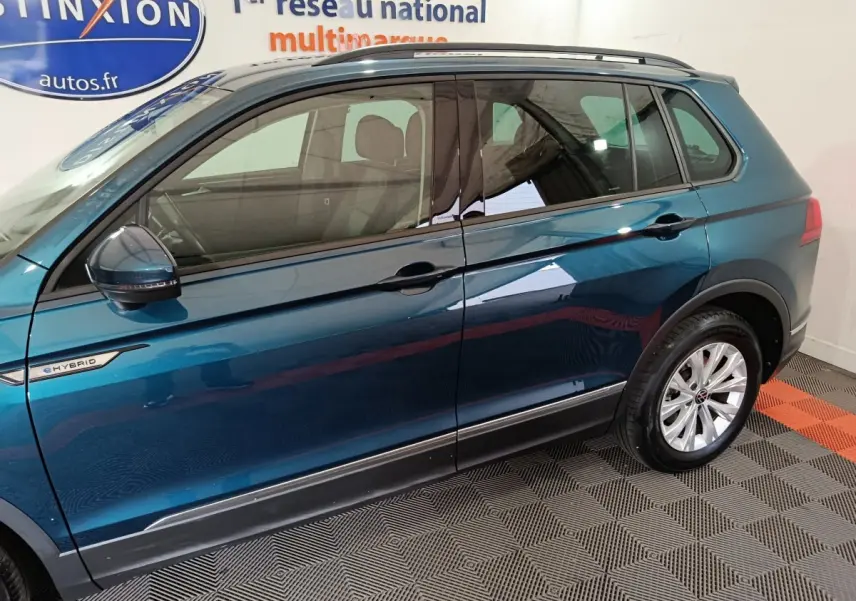 Vue latérale côté gauche d'un Volkswagen Tiguan bleu hybride rechargeable avec badge eHybrid et jantes argentées.