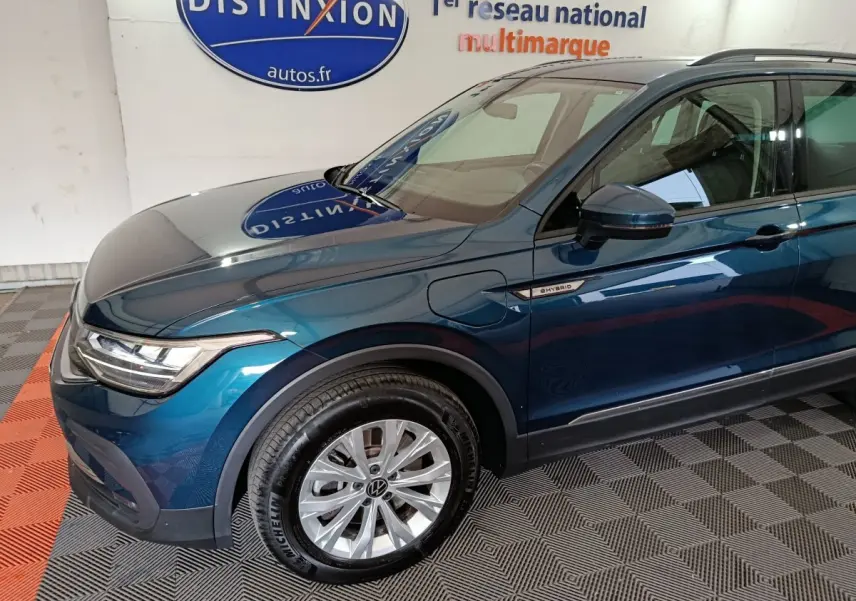Vue 3/4 avant gauche du Volkswagen Tiguan bleu hybride rechargeable avec badge "eHybrid" sur l'aile avant.