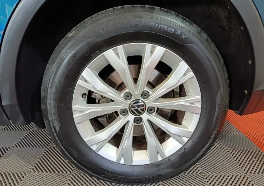 Gros plan sur la roue avant gauche du Volkswagen Tiguan bleu 1.4 eHybrid avec jante en alliage argentée.