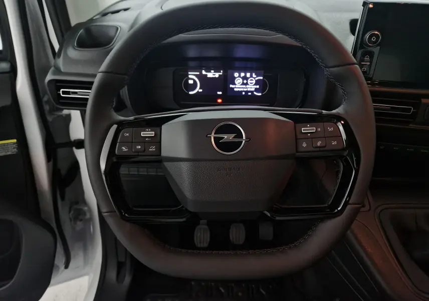 Vue rapprochée du volant noir de l'Opel Combo Life blanc, avec commandes intégrées et tableau de bord numérique éclairé.