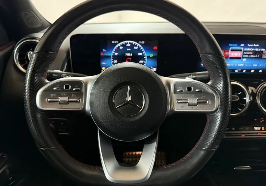 Vue rapprochée du volant cuir noir avec surpiqûres rouges du Mercedes GLB 200 d AMG Line et tableau de bord digital.