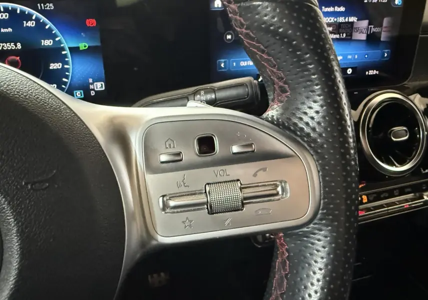 Gros plan sur la partie gauche du volant en cuir perforé du Mercedes GLB 200 d AMG Line, avec commandes audio intégrées.
