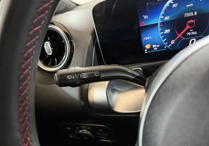 Gros plan sur le commodo de l’essuie-glace et le tableau de bord numérique bleu du Mercedes GLB 200 d AMG Line noir.