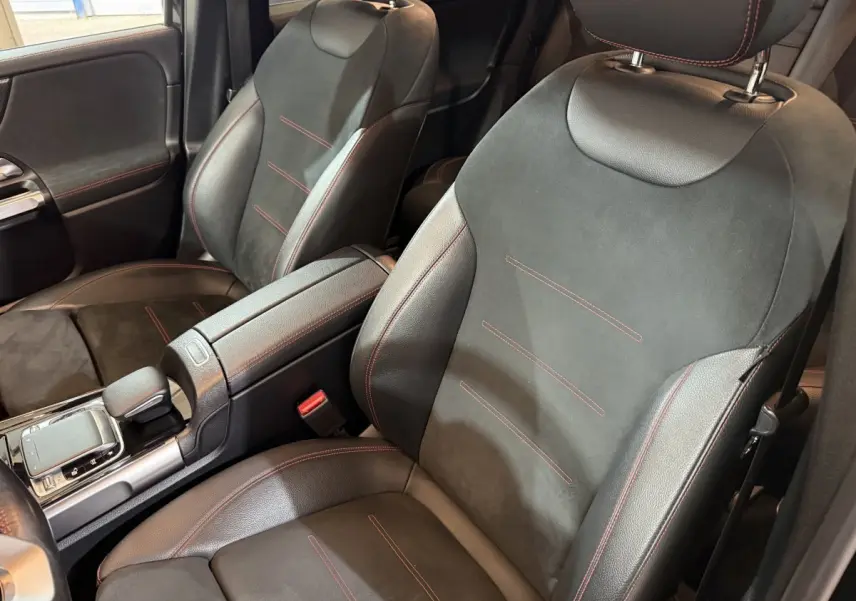 Gros plan sur les sièges avant noirs avec surpiqûres rouges du Mercedes GLB 200 d AMG Line, intérieur moderne et soigné.