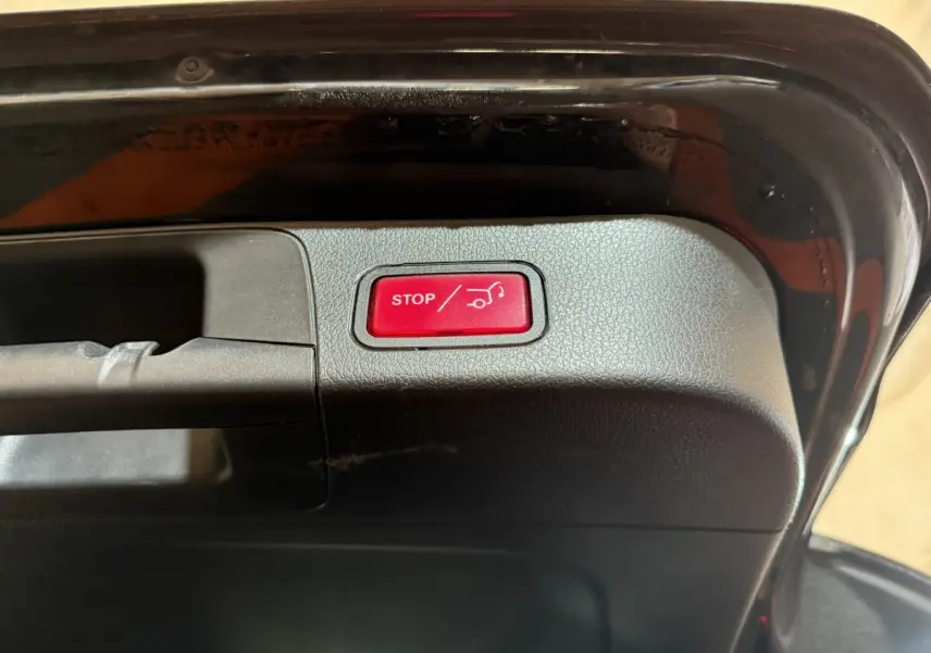Gros plan sur le bouton rouge stop ouverture/fermeture coffre du Mercedes GLB 200 d AMG Line noir, vue intérieure du hayon ouvert.