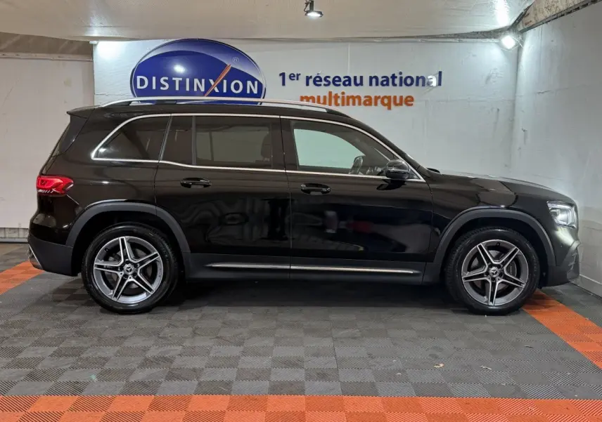 Profil côté gauche d'un Mercedes GLB 200 d AMG Line noir, avec jantes alliage et rails de toit chromés en intérieur showroom.