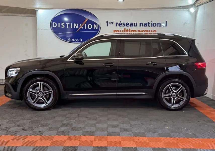 Profil côté gauche d'un Mercedes GLB 200 d AMG Line noir avec jantes alliage et barres de toit chromées en intérieur showroom.