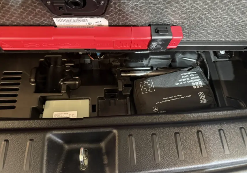 Vue rapprochée du coffre du Mercedes GLB 200 d AMG Line noir, montrant la trousse de premiers secours et le triangle de signalisation.