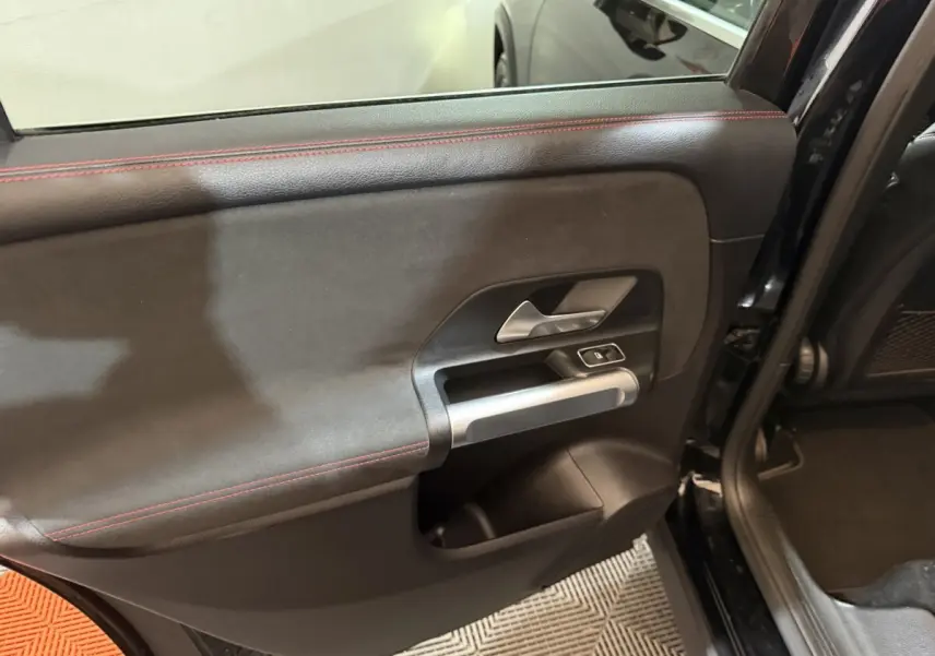 Gros plan sur la porte arrière gauche noire du Mercedes GLB 200 d AMG Line avec surpiqûres rouges et poignée alu.