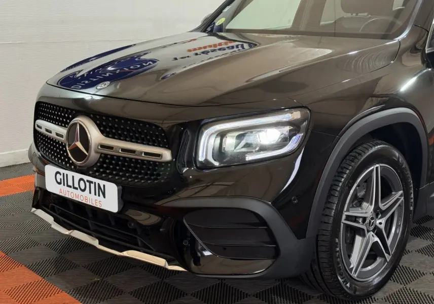 Vue 3/4 avant droit du Mercedes GLB 200 d AMG Line noir avec calandre étoilée et phares LED allumés.
