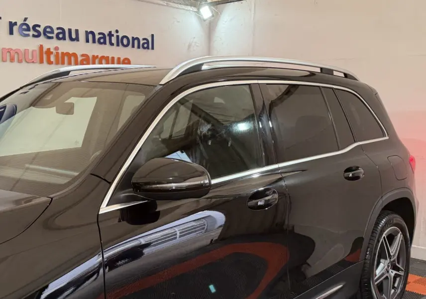 Vue latérale côté gauche d'un Mercedes GLB 200 d AMG Line noir avec barres de toit chromées et jantes alliage cinq branches.