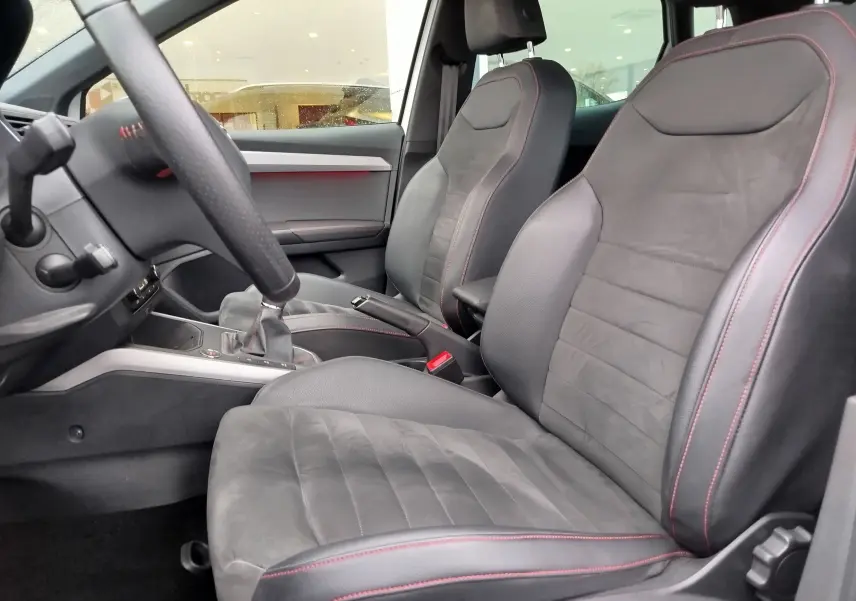 Vue intérieure côté conducteur de la SEAT Arona 2020, sièges en cuir noir avec surpiqûres rouges et volant partiel visible.