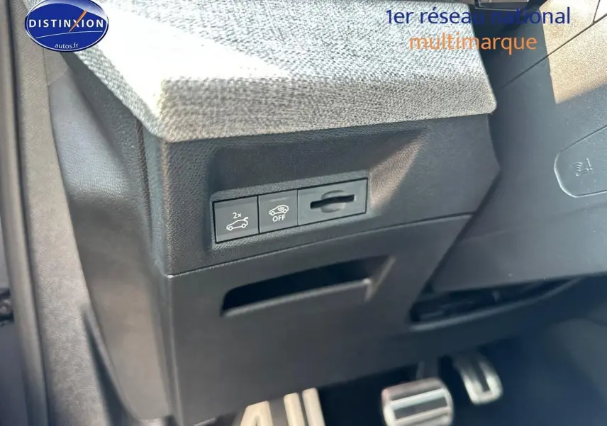 Gros plan sur la partie inférieure gauche du tableau de bord gris avec commandes d'ouverture du coffre et pédalier sport en aluminium.