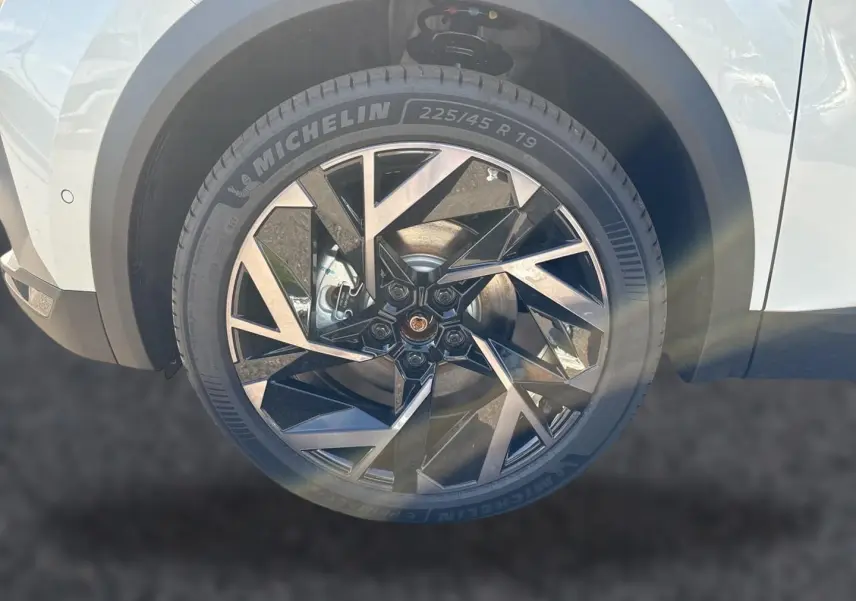 Gros plan sur la roue avant droite blanche nacrée du Renault Symbioz 1.8 e-tech avec jante alu au design géométrique noir et argent.