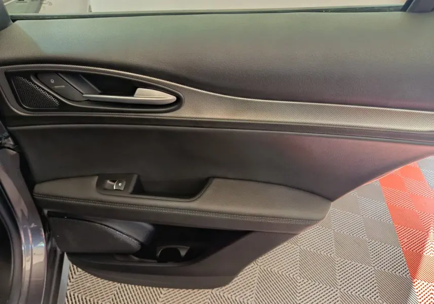 Détail de la porte côté gauche de l'Alfa Romeo Stelvio gris foncé 2024 avec poignée argentée et garniture noire.