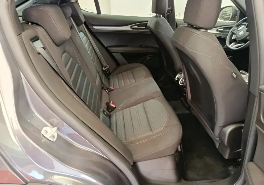 Vue côté gauche arrière de l'habitacle gris foncé de l'Alfa Romeo Stelvio avec sièges tissu et détails intérieurs visibles.