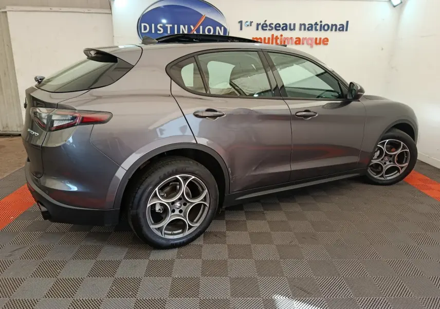 Vue côté gauche d'un Alfa Romeo Stelvio gris foncé 2024 avec jantes spécifiques et feux arrière LED dans un showroom.