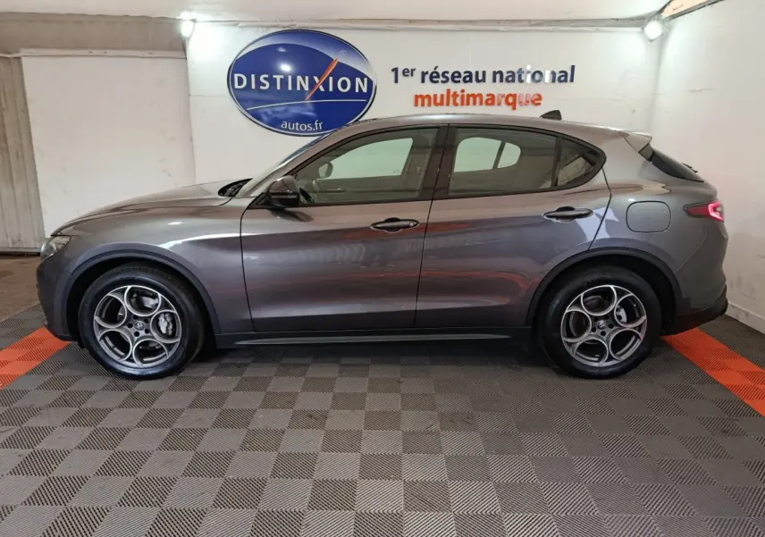 Profil côté gauche d'un Alfa Romeo Stelvio gris foncé 2024, avec jantes distinctives et ligne élancée dans un showroom.