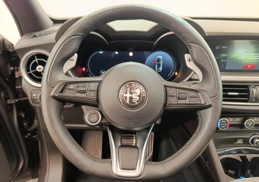 Vue rapprochée du volant cuir noir de l'Alfa Romeo Stelvio 2024 avec tableau de bord digital et commandes intégrées.