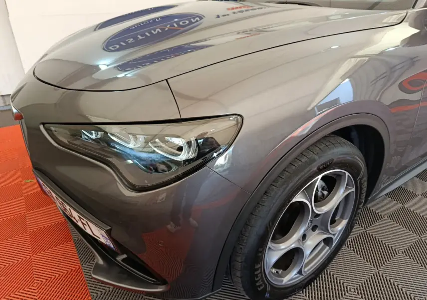 Gros plan sur l'avant droit gris foncé de l'Alfa Romeo Stelvio 2024, mettant en valeur son phare LED et sa jante distinctive.