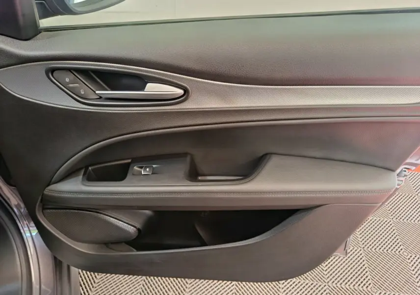 Gros plan sur la porte côté gauche gris foncé de l'Alfa Romeo Stelvio avec poignée argentée et commandes verrouillage.