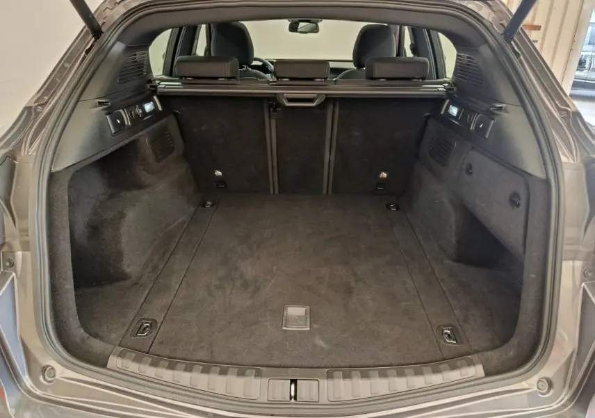 Coffre ouvert vu de l'arrière d'un Alfa Romeo Stelvio gris foncé, intérieur spacieux et tapis noir.