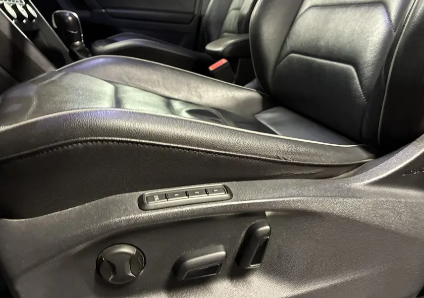 Gros plan sur le siège conducteur en cuir noir du Volkswagen Tiguan 2.0 TDI 150 Carat, avec commandes électriques visibles sur le côté.