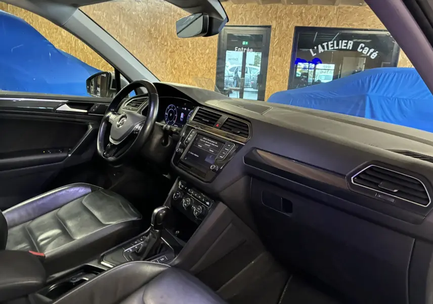 Vue intérieure côté conducteur du Volkswagen Tiguan gris 2017, mettant en valeur le tableau de bord et les sièges en cuir noir.