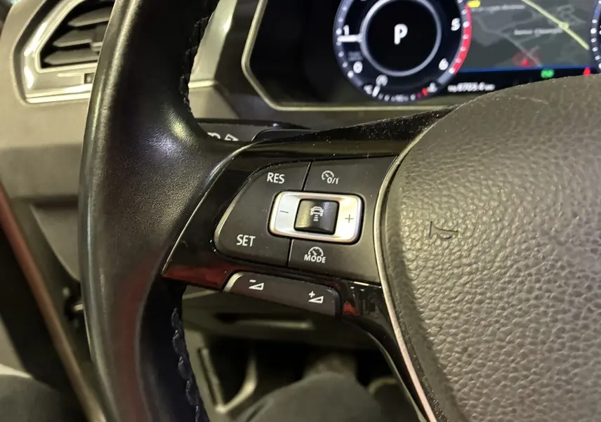 Gros plan sur le volant noir du Volkswagen Tiguan 2.0 TDI 150 Carat, montrant les commandes de régulateur de vitesse à gauche.