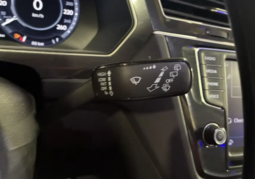 Gros plan sur la commande des essuie-glaces du Volkswagen Tiguan gris, avec tableau de bord et écran multimédia en arrière-plan.