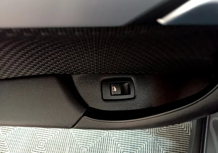 Gros plan sur le bouton d'ouverture électrique du coffre dans l'habitacle d'une BMW X2 gris foncé.