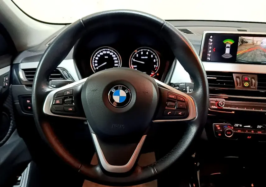 Vue intérieure centrée sur le volant cuir noir de la BMW X2 2021 avec tableau de bord et écran multimédia affichant l'aide au stationnement.