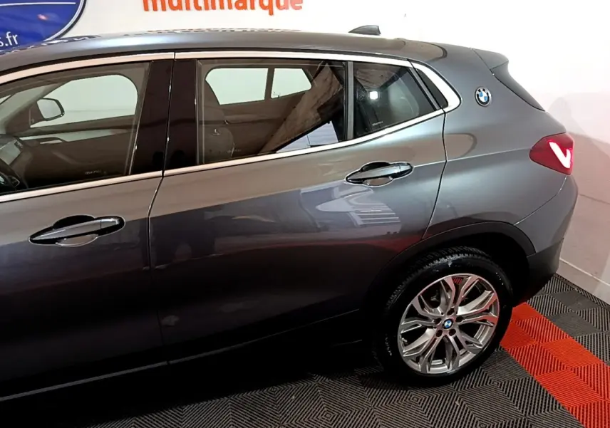 Vue latérale droite d'un BMW X2 gris foncé avec jantes alliage et logo rond sur l'aile arrière.