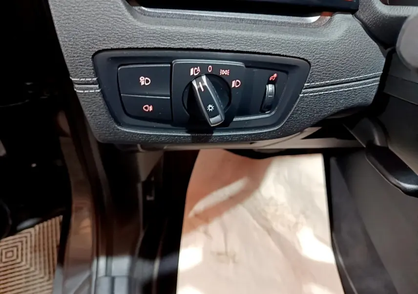 Gros plan sur le bouton de commande des phares dans l'habitacle d'une BMW X2 gris foncé, côté conducteur.