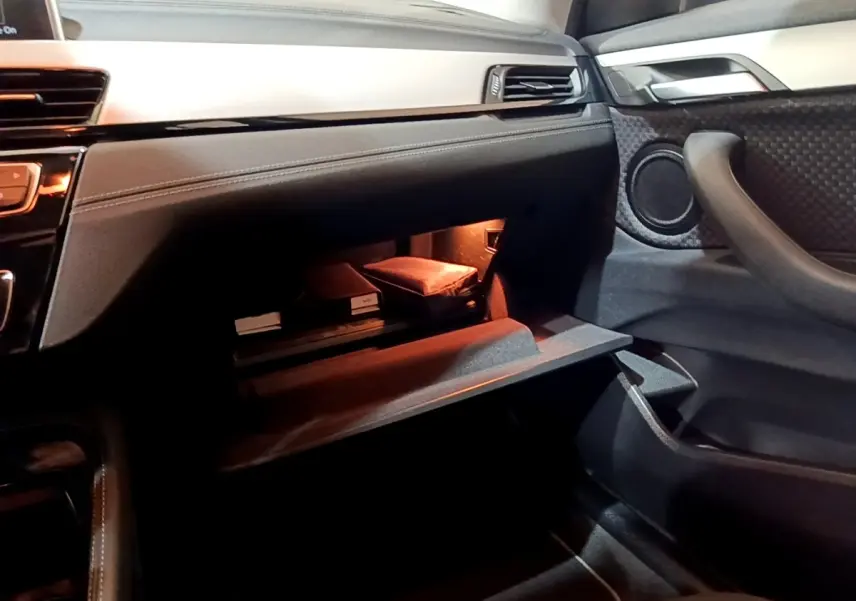 Intérieur BMW X2 sDrive18i 2021, vue côté passager sur boîte à gants ouverte avec éclairage intérieur chaud.