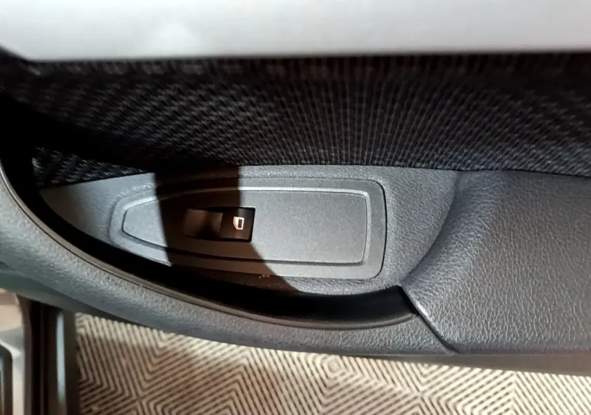 Bouton de commande de lève-vitre sur la porte intérieure côté gauche d'une BMW X2 gris foncé, vue rapprochée.