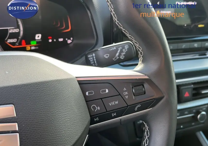 Gros plan sur le volant noir avec surpiqûres blanches du SEAT Arona 2025, montrant les commandes multifonctions côté droit.