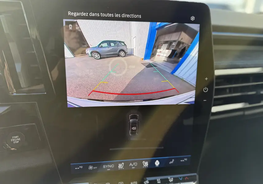 Écran de caméra de recul du Renault Austral blanc nacré avec toit noir, vue arrière sur un parking et un bâtiment bleu.