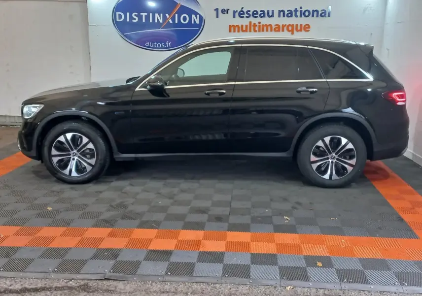 Profil côté gauche d'un Mercedes GLC 300 E Business Line hybride rechargeable noir, stationné en intérieur sur sol damier.