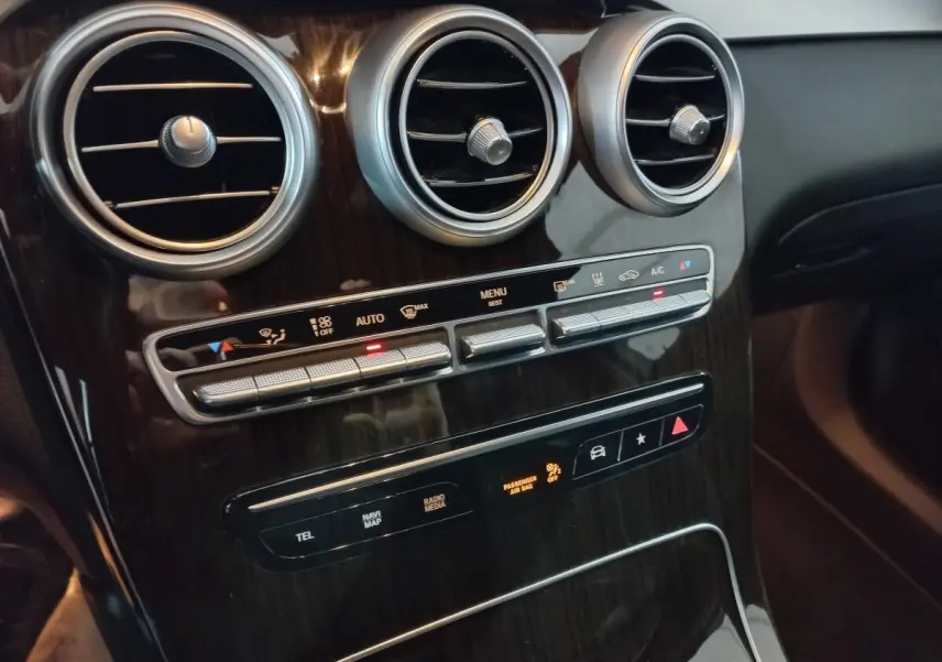 Vue rapprochée du tableau de bord noir brillant avec aérateurs ronds et commandes climatisation du Mercedes GLC 300 E Business Line.