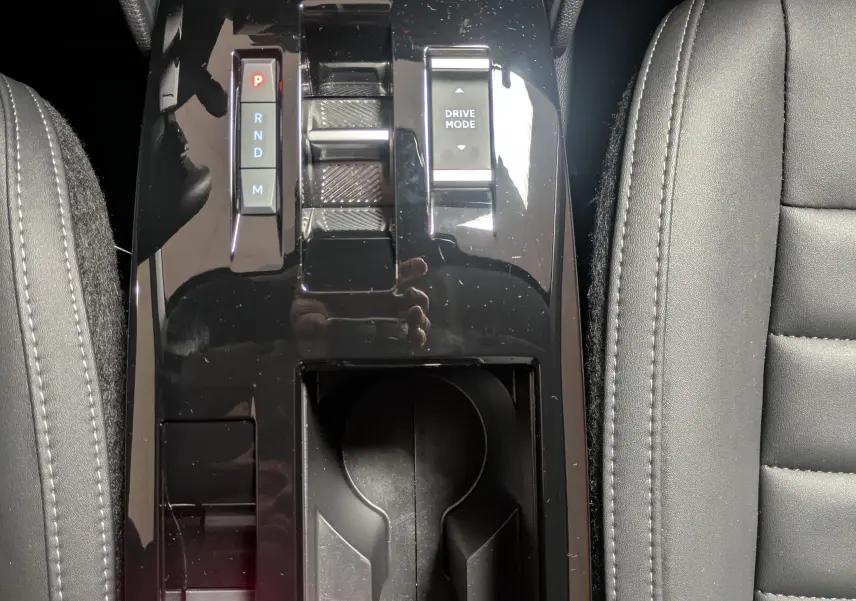 Vue plongeante sur la console centrale noire brillante de la Citroën C4 hybride 2025 avec levier de vitesses et bouton Drive Mode.